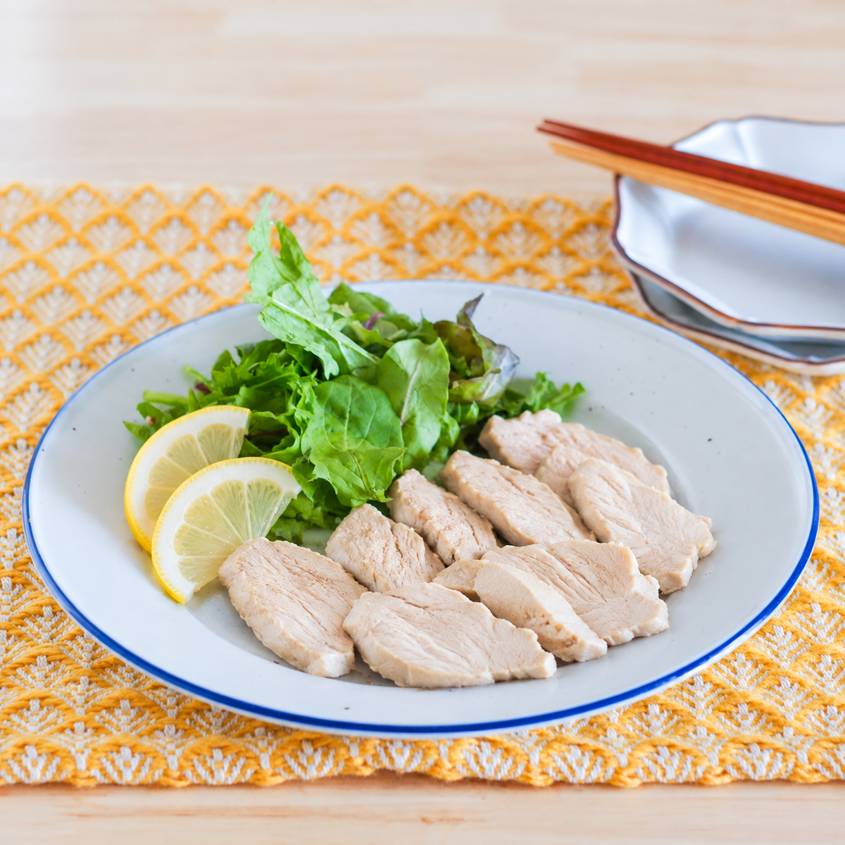 加熱した鶏むね肉のスライスにレモンと葉野菜を添えたイメージ（AI生成）