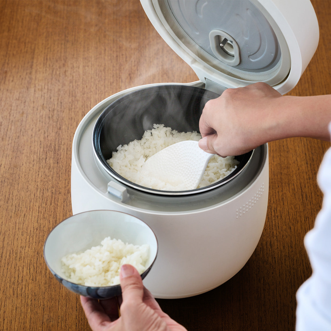 HUG 炊飯器 ホワイトから炊きたてのごはんをよそう使用シーン